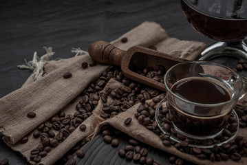 Fototapeta na wymiar Cup of coffee and coffee beans roating with old wooden scoop and coffee beans around on the wooden and dark stone background. Oblique view from the top with copy space for your text.