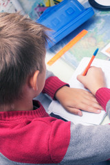 A boy writes English words by hand on traditional white paper in a notebook. The boy writes his...
