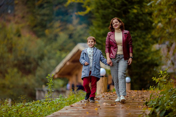 Fototapeta premium Travelers mother and son on a walk in the autumn mountains against the background of a wooden house from a log house