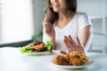 Woman on dieting for good health concept, young women use hands to push fried chicken and choose to eat vegetables for good health. - obrazy, fototapety, plakaty