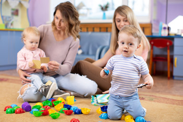 Children 1 year age play in kindergarten or club centre under the supervision of moms