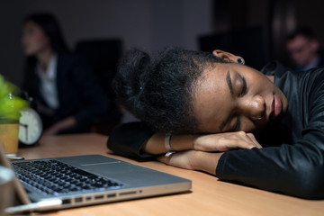 African businesswoman falls asleep because she is tired of working overtime in the office to complete the project within the time limit.