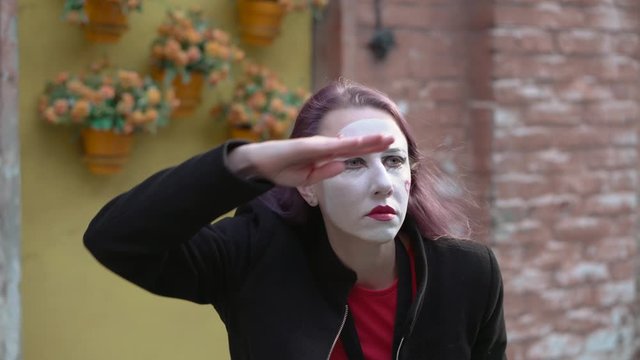 Mime girl in a black coat put a hand to her eyes in a search around herself.