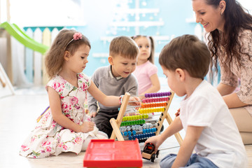 Kindergarten teacher and kids playing with abacus sitting on the floor in daycare