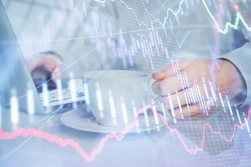 Double exposure of graph with man typing on computer in office on background. Concept of hard work.