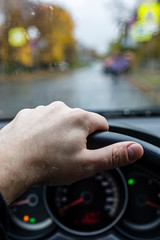 Hand of driver on steering wheel in city in rainy weather