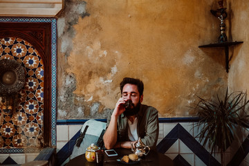 .Young handsome tourist enjoying a moment alone in a Moroccan style tea shop. Drinking traditional...