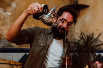 .Young handsome tourist enjoying a moment alone in a Moroccan style tea shop. Drinking traditional tea and eating typical Arabic sweets. Travel around the world. Lifestyle