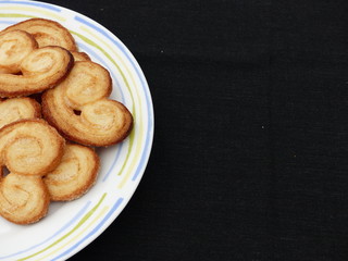 Heart-shaped puff pastry (palmeritas) on a white plate with a black background. (negative space)
