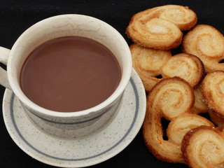 Heart-shaped puff pastry (palmeritas) with a white cup of chocolate with a black background