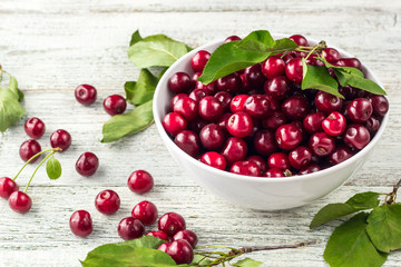 Fresh sweet cherries white bowl with leaves in water drops on wooden background