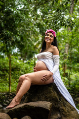 Happy young hispanic pregnant woman wearing white dress with belly showing sitting outdoors in Guatemala