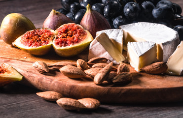 Cheese plate served with grapes, figs and nuts on a wooden background.