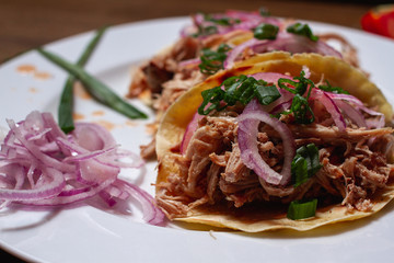 tres tacos de carne de cerdo en un plato blanco sobre una mesa de madera