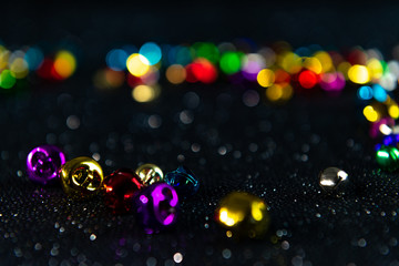 Multi-colored Christmas jingle bells. Black blurred bokeh glitter background. Shallow depth of field. For overlay, background or texture.