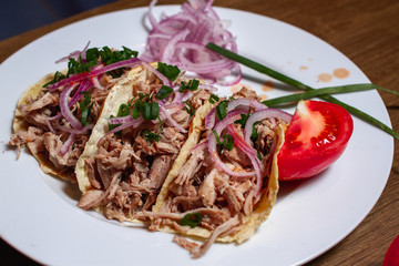 tres tacos de carne de cerdo en un plato blanco sobre una mesa de madera