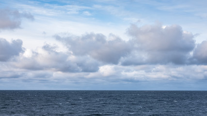 Naklejka na ściany i meble Cloudy blue sky above a blue surface of the sea