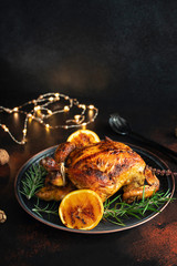 Roasted whole chicken for Christmas or New Year on a dark background with Christmas decorations. Baked Chicken with Oranges and rosemary. Christmas dinner. Space for text. Selective focus. Vertical