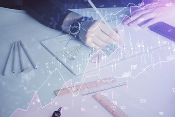 Double exposure of man's hands writing notes of stock market with forex chart.