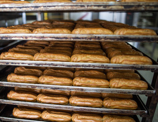 Many custard eclair cakes with butter cream and condensed milk lie on racks in the confectionery industry. Making desserts and sweets on an industrial scale, industry, background