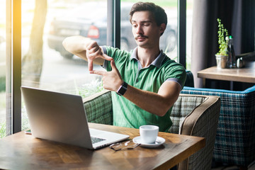 Focus on goals work. Young serious businessman in green t-shirt sitting and looking at laptop screen with crop composition gesture. business goals concept. indoor shot near big window at daytime.