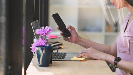 Cropped shot young woman using laptop computer and smartphone.