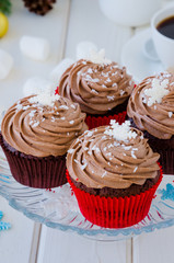 Chocolate cupcakes with cheese chocolate cream with a cup of coffee and marshmallows  for Christmas and New Year on a white wooden background.