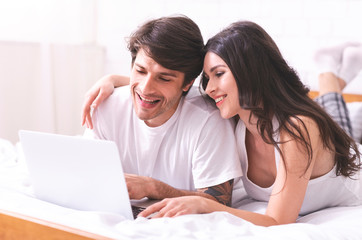 Young married couple lying on bed at home and using laptop