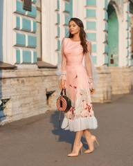 Young pretty woman wearing elegant pink dress on a sunny evening. Beautiful girl with long wavy...
