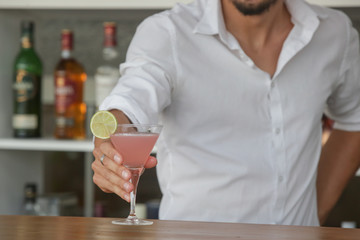 Barman serving a glass of Cosmopolitan drink on the bar counter
