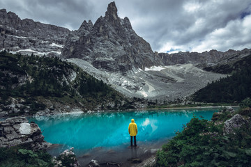 Man in yellow jacket standing alone on the rock at alpine lake Lago di Sorapis in the Italian...