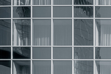 Glass wall with another building reflection. Windows are closed with curtains. Toned for black and white.