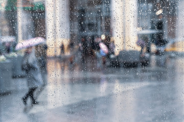 Girl under the umbrella, rainy weather, abstract, blurred motion. View through glass window with rain drops on glass