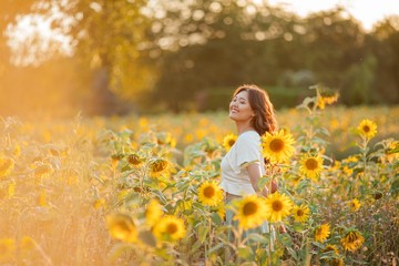 Fototapeta na wymiar Young Asian woman with curly hair in a field of sunflowers at sunset. Portrait of a young beautiful asian woman in the sun.