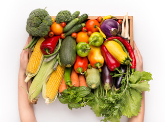 Woman holding big wooden box with fresh vegetables on white