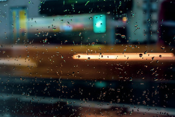 Abstract blurred colorful background. View through glass window with rain drops on bokeh city lights, night street scene