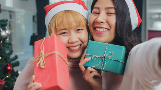 Asian Lesbian couple celebrate Christmas festival. LGBTQ female teen relax happy holding Gift and using smartphone selfie with Christmas tree enjoy xmas winter holidays in living room at home.