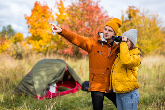 travel, trekking and hiking concept - couple hikers with binoculars posing near green tent in autumn forest