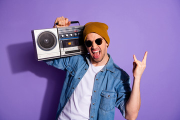Photo of trendy stylish white screaming man holding retro recorder with hands showing you rock sign shouting wearing denim t-shirt cap headwear isolated purple bright color background
