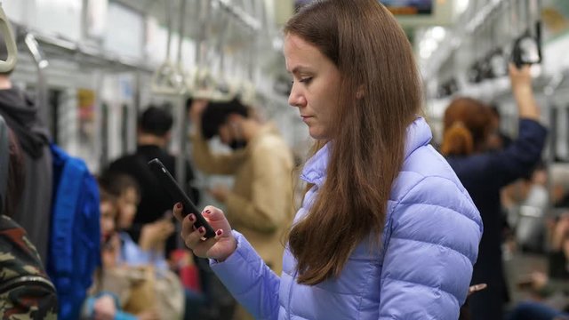 Pensive woman ride at Seoul subway, standing and staring to phone. European tourist travel by public transport. Portrait shot, blurred background, rather empty metro car