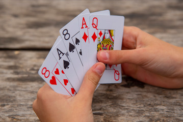 Playing cards in human hands on a wooden background.