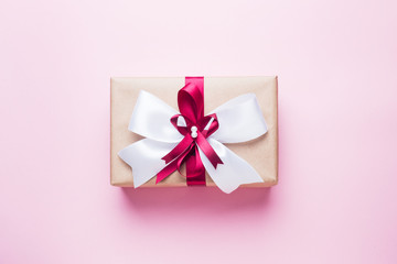 Gift or present box with a big bow on a pink table top view. Flatlay composition for Christmas birthday, mother day or wedding.