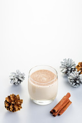 Traditional Christmas cocktail Eggnog with eggs, alcohol, grated nutmeg and cinnamon closeup, copy space, vertical frame. Sweet traditional drink on grey table with beige decorations and pine cones