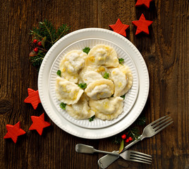 Christmas dumplings stuffed with mushroom and cabbage on a white plate on a rustic wooden table, top view. Traditional Christmas eve dish in Poland