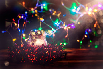 Christmas background. New Year holiday background with copy space. Glass jar full of Christmas decoration toys against Xmas tree bokeh lights