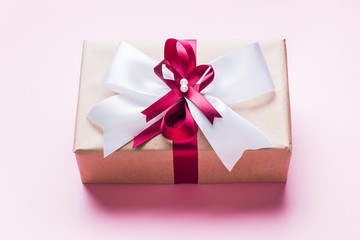 Gift or present box with a big bow on a pink table top view. Flatlay composition for Christmas birthday, mother day or wedding.