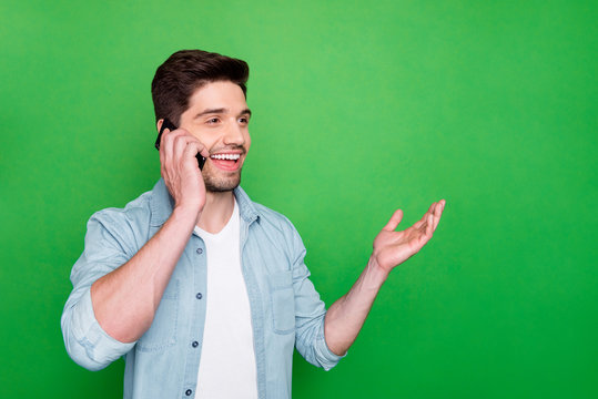 Photo of handsome guy holding telephone hand near ear listen best friend humorous story overjoyed good connection wear denim shirt isolated green color background