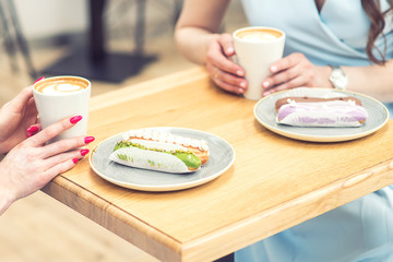 Female hands have a cups of coffee and a plate of eclairs on a table at cafe. The girls at the table with eclairs, a cup of coffee in the hands.