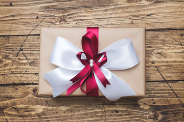 Gift or present box with a big bow on a wooden table top view. Flatlay composition for Christmas birthday, mother day or wedding.
