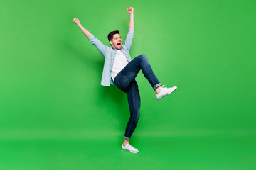 Full body profile photo of carefree crazy guy yelling celebrating favorite football team victory raise fists and leg wear denim shirt isolated green color background